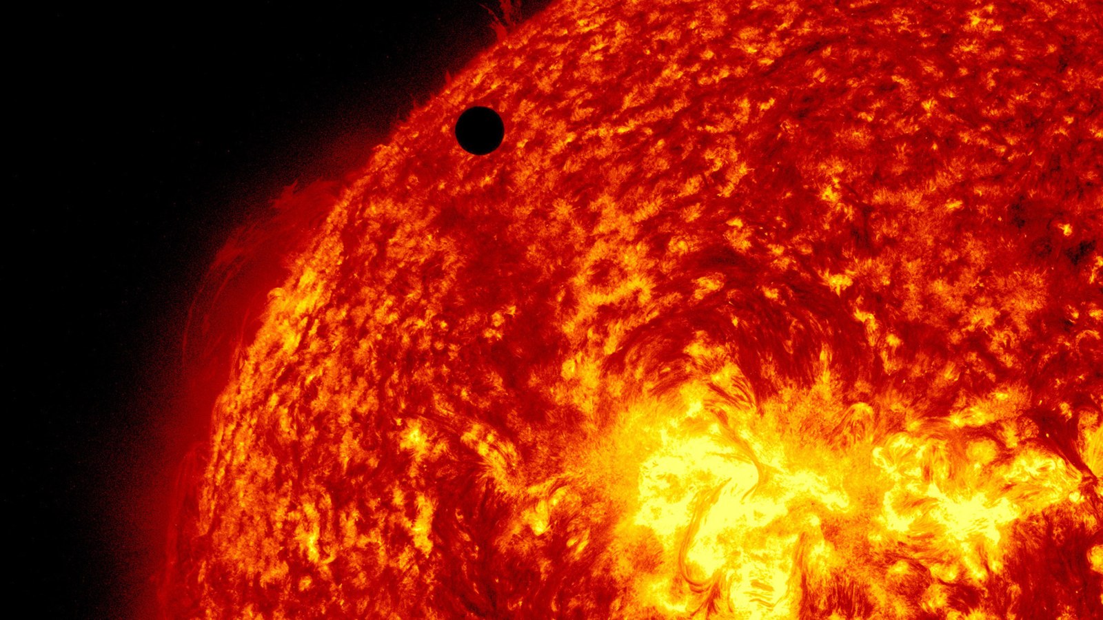 A black object behind the fiery red planet of Venus.
