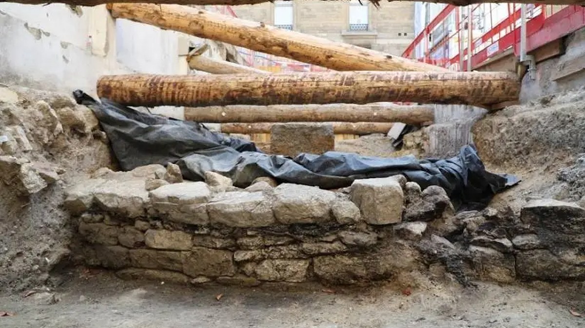 a small stone wall in the foreground with an archaeological tarp and wooden bolsters in the background