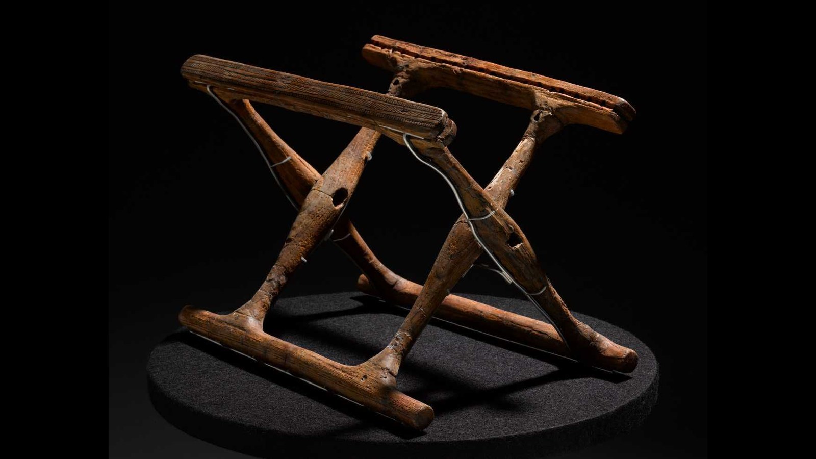 a folding chair base of two wooden squares hitched together at a 45-degree angle against a black background