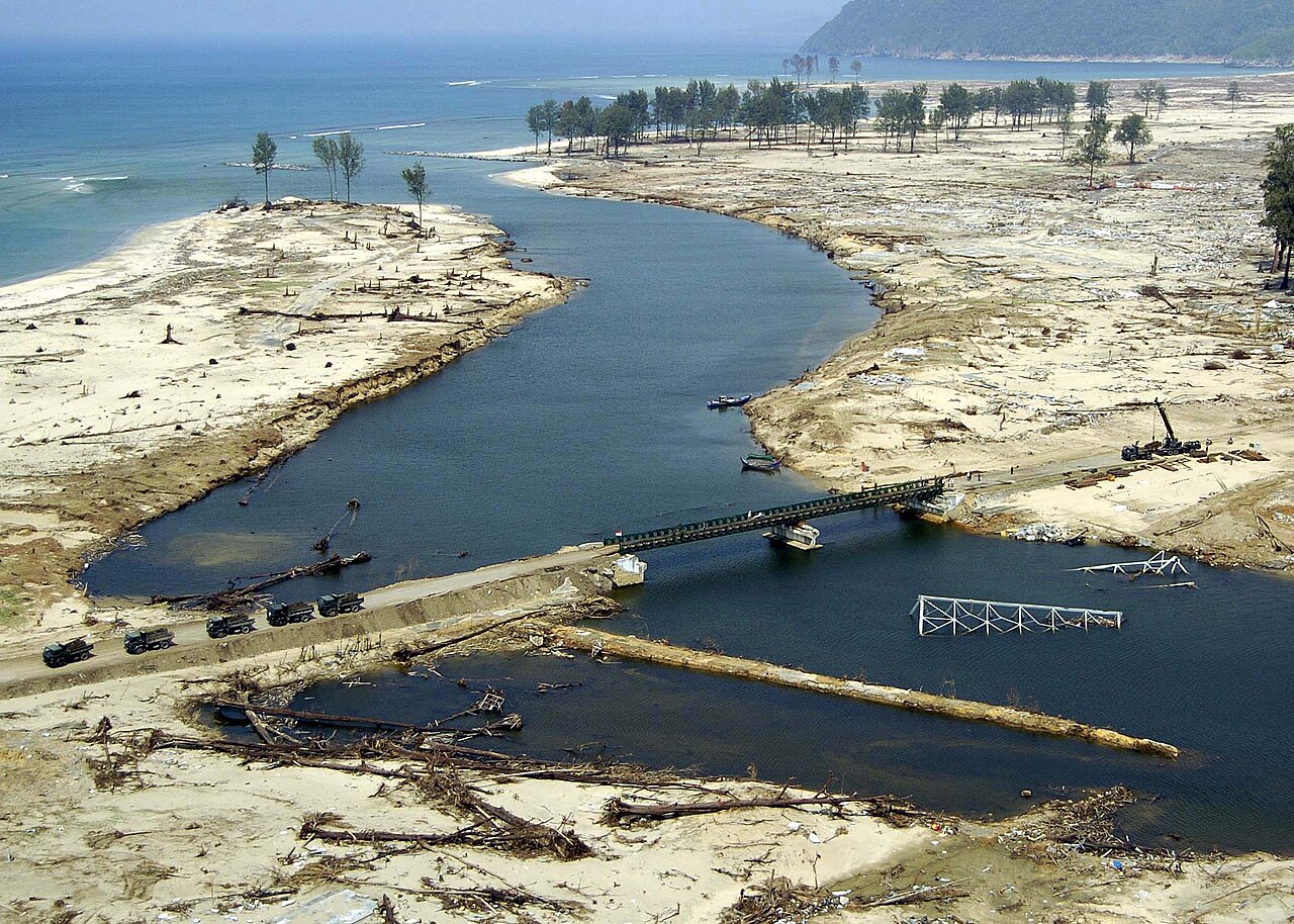 Banda Aceh, Sumatra, Endonezya (27 Ocak 2005) - Banda Aceh, Sumatra, Endonezya yakınlarında geçmek için yakın zamanda yeniden inşa edilen bir köprünün yakınında kamyonlar sıraya girerken, bir Tsunamide yıkılan eski köprü yanındaki bir nehirde yatıyor.
